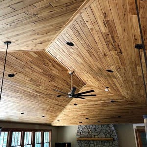 May include: A wooden ceiling with a complex, angled design. The ceiling is constructed from light brown wooden planks, with recessed lighting and a ceiling fan. Two pendant lights hang from the ceiling.