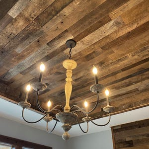 May include: A rustic wooden ceiling with a chandelier featuring a distressed wood finish and six light bulbs. The chandelier has a black metal frame and is hanging from the ceiling.