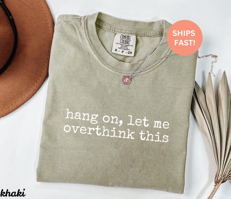May include: A khaki green t-shirt with the text "hang on, let me overthink this" printed in white. The shirt is made of a soft, comfortable material.