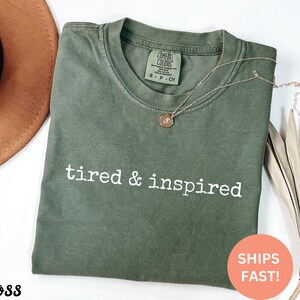 May include: A green t-shirt with the text "tired & inspired" in white lettering. The shirt is made of a soft, comfortable material.