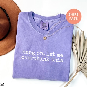 May include: A purple t-shirt with the text "hang on, let me overthink this" printed in white. The shirt is made of a soft, comfortable material.