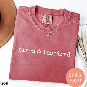 May include: Crimson red t-shirt with the text "tired & inspired" in white lettering.