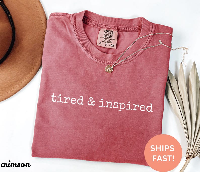 May include: Crimson red t-shirt with the text "tired & inspired" in white lettering.