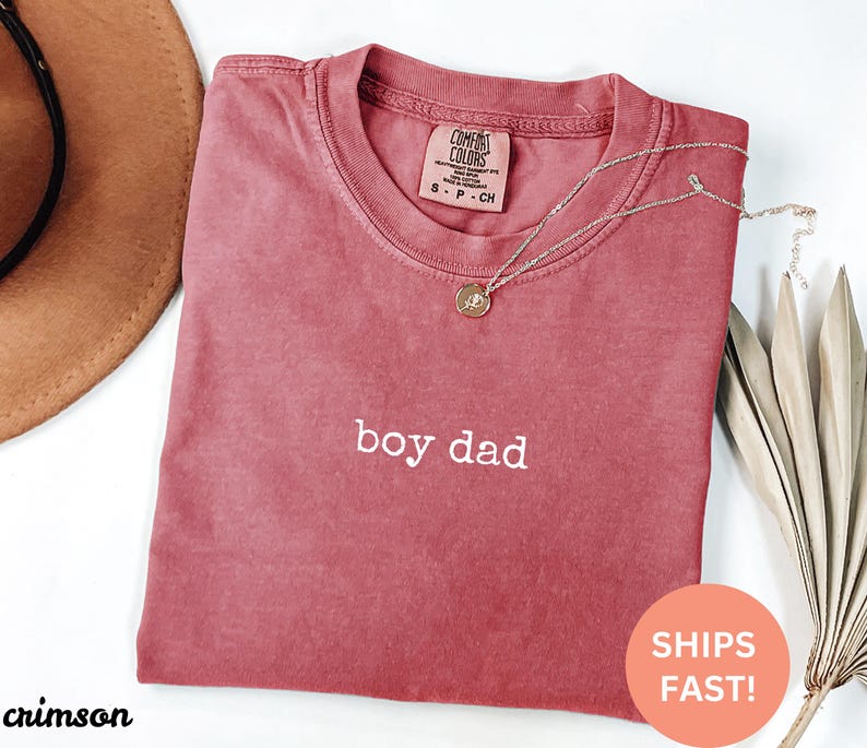 May include: Crimson red t-shirt with the text "boy dad" in white lettering.