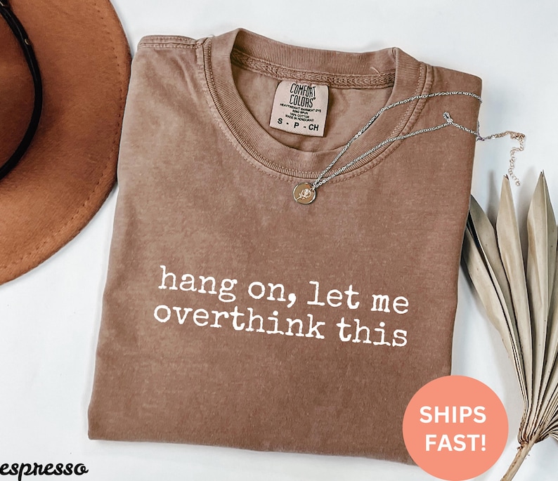 May include: A brown t-shirt with the text "hang on, let me overthink this" printed in white.