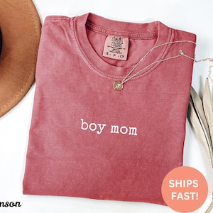 May include: Crimson red t-shirt with the text "boy mom" embroidered in white. The shirt is made of a soft, comfortable fabric and has a relaxed fit.