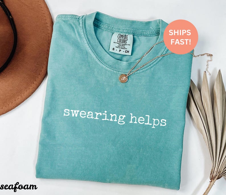 May include: Seafoam green t-shirt with the text "swearing helps" printed in white on the front.