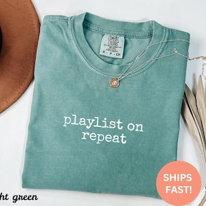 May include: Light green t-shirt with the text "playlist on repeat" in white. The shirt is made of a soft, comfortable material.