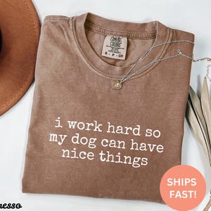 May include: A brown t-shirt with the text "i work hard so my dog can have nice things" printed in white.