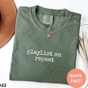 May include: Green t-shirt with the text "playlist on repeat" in white lettering.