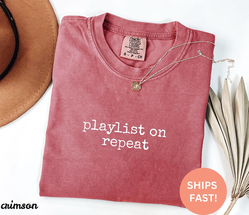 May include: Crimson red t-shirt with the text "playlist on repeat" in white. The shirt is made of a soft, comfortable material.