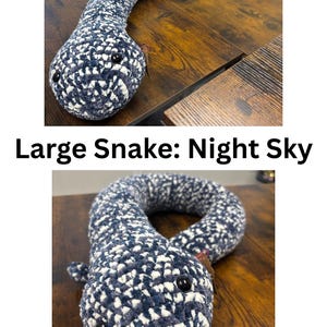 May include: A long, plush, crocheted snake toy featuring a variegated pattern of dark navy blue and white yarn. The snake has two smooth, round black plastic eyes and a soft, stuffed body that curves along the surface. The text Large Snake: Night Sky.