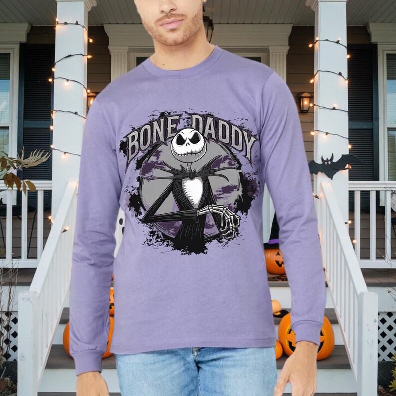 Może przedstawiać: Fioletowy T-shirt z długim rękawem z grafiką Jacka Skellingtona z filmu Koszmar przed świętami. Grafika zawiera tekst "Bone Daddy".