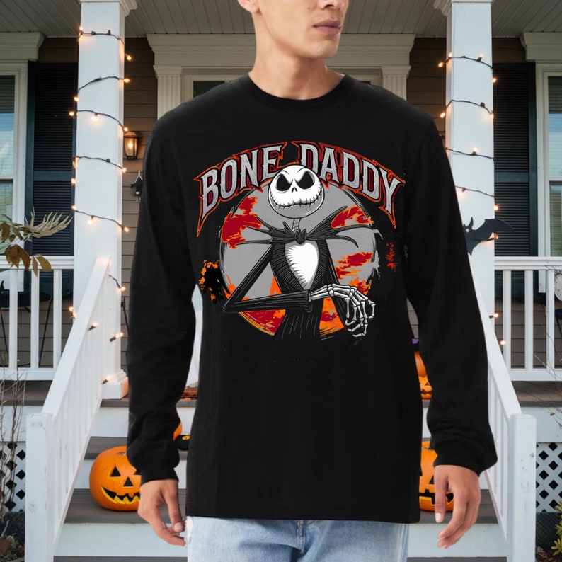 Może przedstawiać: Czarny T-shirt z długim rękawem z grafiką Jacka Skellingtona z filmu Koszmar przed świętami. Grafika przedstawia Jacka Skellingtona z tekstem "Bone Daddy" wok&oacute;ł niego.