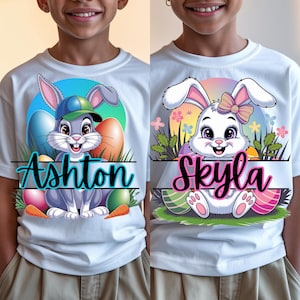May include: Two white t-shirts with Easter bunny graphics. The bunny on the left is gray with a blue baseball cap and the text "Ashton". The bunny on the right is white with a pink bow and the text "Skyla".