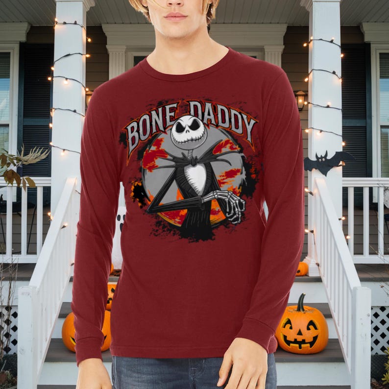 Może przedstawiać: Czerwona koszula z długim rękawem z grafiką Jacka Skellingtona z filmu Koszmar przed świętami. Grafika zawiera napis "Bone Daddy".