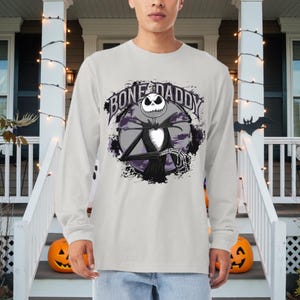 Może przedstawiać: Szary T-shirt z długim rękawem z grafiką Jacka Skellingtona z filmu Koszmar przed świętami. Grafika zawiera tekst "Bone Daddy".
