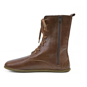 Op de afbeelding: Bruine leren enkellaarsjes met een vetersluiting aan de voorkant en een zijrits. De laarzen hebben een platte zool.