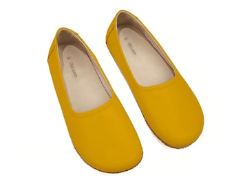 May include: A pair of mustard yellow ballet flats. The shoes have a rounded toe and a low profile. The interior of the shoe is a light beige colour. The brand name "Old Loom" is printed on the insole.