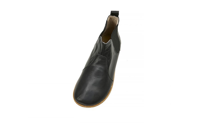 K&ouml;nnte beinhalten: Schwarze Lederstiefeletten mit abgerundeter Spitze und elastischen Seitenteilen. Die Stiefeletten haben eine braune Gummisohle.