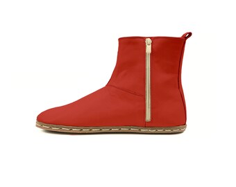 May include: A red ankle boot with a side zipper and a pull tab. The boot has a stitched sole and a low heel. The zipper is gold-colored. The boot is made of a smooth material and is likely leather.