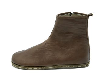 May include: A brown leather ankle boot with a zipper closure. The boot has a rounded toe and a stitched sole. The upper is a solid brown color, and the boot appears to be made of soft leather. The boot is designed for everyday wear.