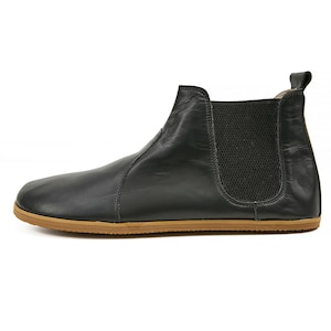 K&ouml;nnte beinhalten: Schwarze Lederstiefel mit brauner Gummisohle. Die Stiefel haben ein elastisches Panel an der Seite und eine Lasche an der R&uuml;ckseite.