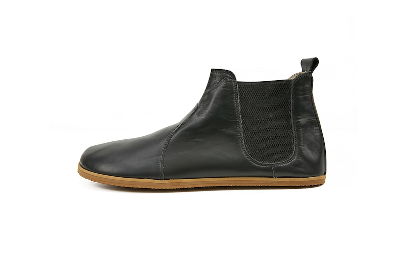 K&ouml;nnte beinhalten: Schwarze Lederstiefel mit brauner Gummisohle. Die Stiefel haben ein elastisches Panel an der Seite und eine Lasche an der R&uuml;ckseite.