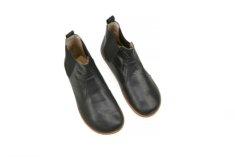 K&ouml;nnte beinhalten: Ein Paar schwarze Leder-Stiefeletten mit einem Schlupf-Design und einer abgerundeten Spitze.