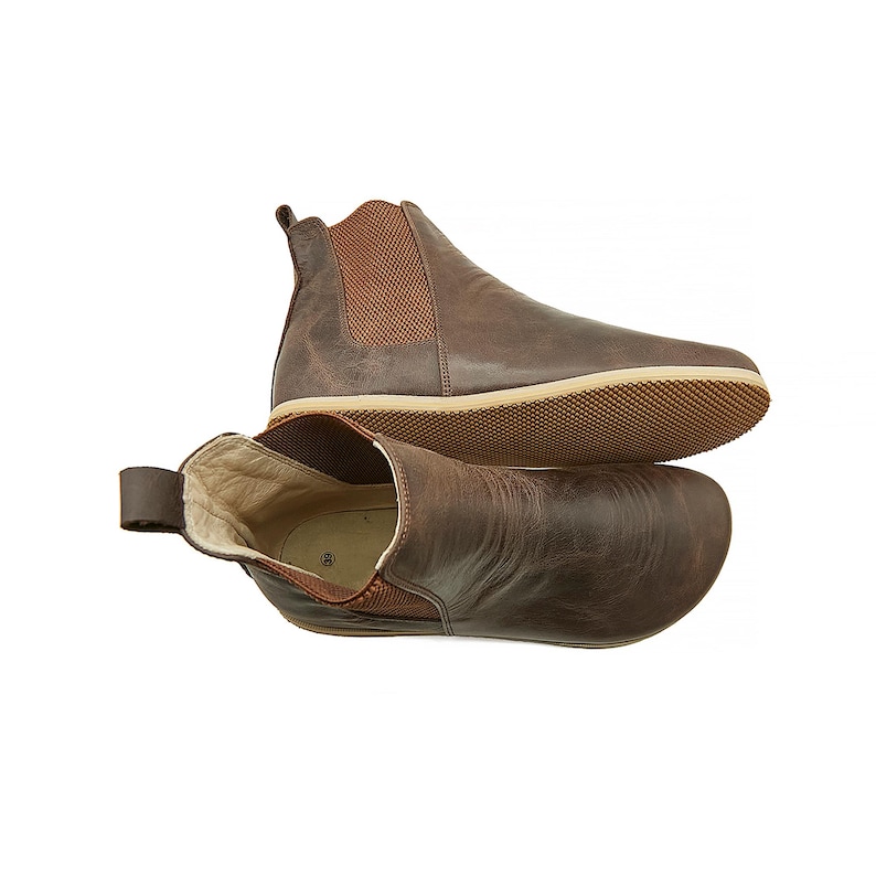 May include: A pair of brown leather ankle boots with elastic side panels. The boots have a rounded toe and a flat sole.