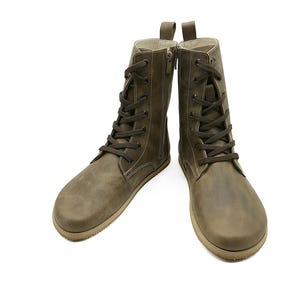 May include: A pair of olive green leather boots with laces and zips. The boots have a round toe and a pull tab at the top. The soles are a light brown colour. The boots are displayed against a white background.