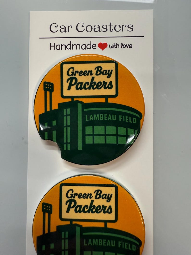 Puede incluir: Dos posavasos redondos para coche con el logotipo de los Green Bay Packers y el estadio Lambeau Field. Los posavasos tienen un fondo naranja con un dise&ntilde;o de estadio verde y negro. El texto "Car Coasters" y "Handmade with love" est&aacute; en la parte superior.