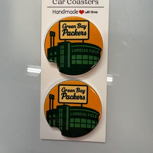 Puede incluir: Dos posavasos redondos para coche con el logotipo de los Green Bay Packers y el dise&ntilde;o del estadio Lambeau Field. Los posavasos son de color naranja y verde, con las palabras "Green Bay Packers" y "Lambeau Field". Hechos a mano.