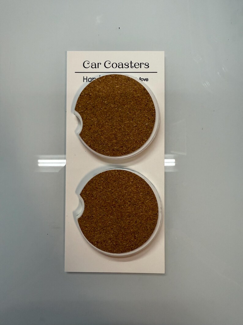 Puede incluir: Dos posavasos para coche con centro de corcho y borde de pl&aacute;stico transparente, expuestos en una tarjeta blanca. La tarjeta dice "Car Coasters" en la parte superior. Los posavasos est&aacute;n dise&ntilde;ados para caber en el portavasos de un coche.