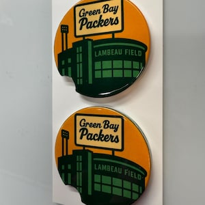 Puede incluir: Dos posavasos para coche con el logotipo de los Green Bay Packers y el estadio Lambeau Field sobre un fondo naranja. Los posavasos son redondos con un recorte curvo. El texto "Car Coasters" y "Handmade with love" est&aacute; en la parte superior.