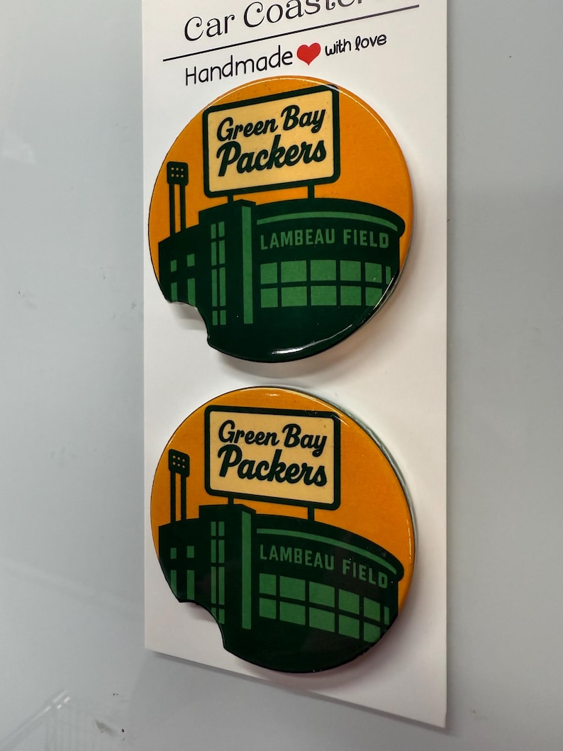Puede incluir: Dos posavasos para coche con el logotipo de los Green Bay Packers y el estadio Lambeau Field sobre un fondo naranja. Los posavasos son redondos con un recorte curvo. El texto "Car Coasters" y "Handmade with love" est&aacute; en la parte superior.