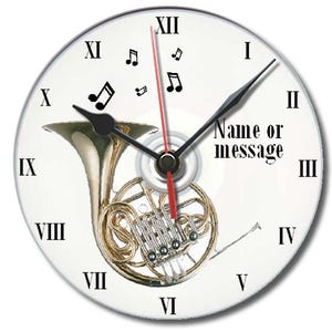 Könnte beinhalten: Ein weißes Zifferblatt mit schwarzen römischen Ziffern und Zeigern. Ein Messing-Waldhorn ist zentriert, mit Noten verstreut. Der Text "Name or message" ist auf dem Zifferblatt aufgedruckt.