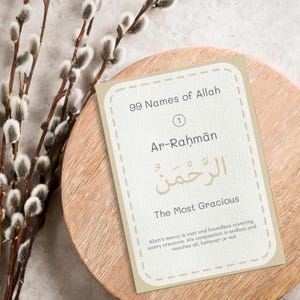 May include: A card with the text "99 Names of Allah" and the name "Ar-Rahman" in Arabic script, meaning "The Most Gracious." The card is beige with a dashed border, resting on a wooden surface, with pussy willow branches.