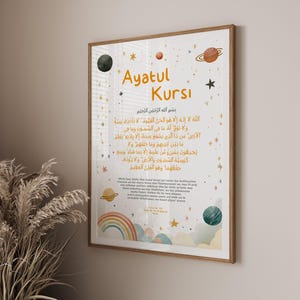 Könnte beinhalten: Gerahmter Druck mit dem Text "Ayatul Kursi" in goldfarbenen Buchstaben. Das Kunstwerk zeigt ein himmlisches Thema mit Planeten, Sternen und einem Regenbogen. Der Hintergrund ist eine weiche, neutrale Farbe, und der Rahmen ist aus hellem Holz.