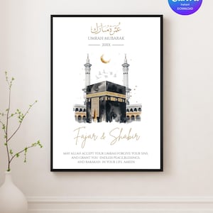 May include: A framed Umrah Mubarak print featuring a watercolor illustration of the Kaaba, a crescent moon, and minarets. The print includes the text "Umrah Mubarak" and "Fajar & Shabir", along with a prayer. The Canva logo is in the upper right corner.