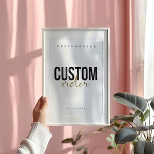 May include: White framed print with the words "CUSTOM order" in black and gold lettering. The text "DESIGNMARK8" and "BY SOMERA" are also visible. The print is held up against a pink background.
