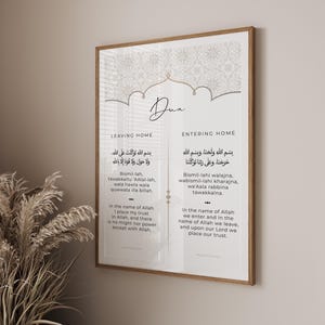 以下が含まれることがあります： アラビア語カリグラフィーと英語翻訳が施された額入りのプリント。アートワークは、2つのテキスト列の上にエレガントなスクリプトで「Dua」という単語を特徴としています。左側は「Leaving Home」、右側は「Entering Home」です。フレームはライトブラウンです。
