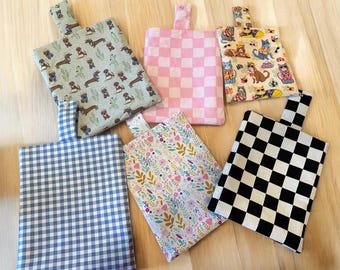 May include: Six reusable shopping bags with different patterns. The bags are made of fabric and have a handle on top. The patterns include a blue and white gingham, a black and white checkered pattern, a pink and white checkered pattern, a floral pattern, a pattern with dogs, and a pattern with cats.