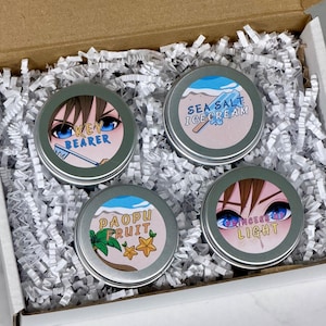 May include: A gift box filled with white paper shreds, containing four round, silver-colored tins. Each tin has a colorful label with anime-style character eyes and text: "Key Bearer", "Sea Salt Ice Cream", "Paopu Fruit", and "Princess Light".