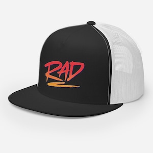 May include: A black and white trucker hat with a black front panel and a white mesh back panel. The front panel features a red, orange, and yellow graphic of the word "RAD" in a stylized font.
