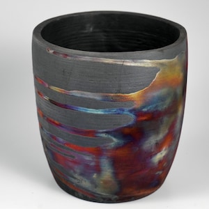 Puede incluir: Un jarrón de cerámica negro con una superficie texturizada y vetas iridiscentes azules, rojas y naranjas.