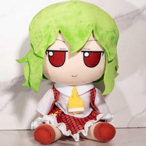 Può includere: Una bambola di peluche con capelli verdi, occhi rossi e una camicia bianca con una cravatta gialla. La bambola ha una gonna a quadri rossa e piedi rossi. La bambola è seduta.