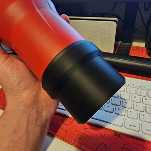 Puede incluir: Una botella de agua roja aislada con una base negra. La botella la sostiene una persona. La marca "Milwaukee" es visible en la botella. La botella es cil&iacute;ndrica y parece ser de metal.