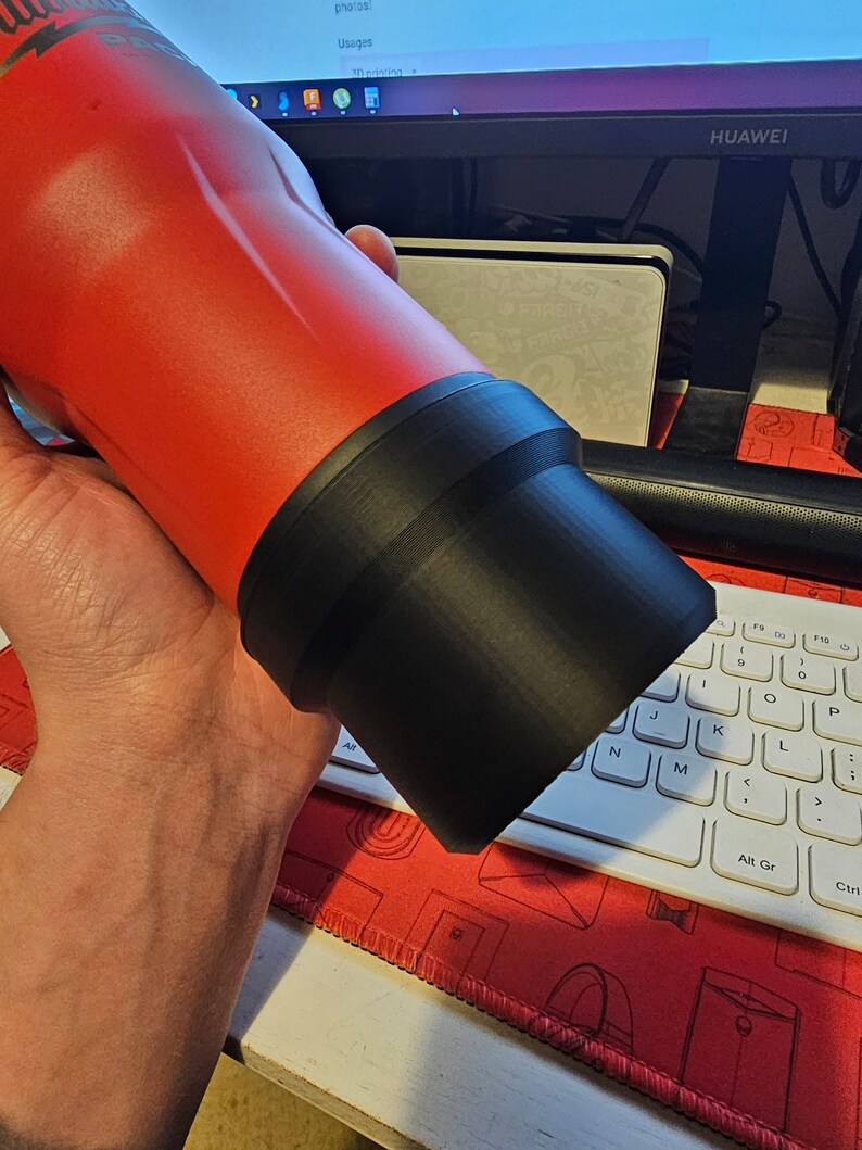 Puede incluir: Una botella de agua roja aislada con una base negra. La botella la sostiene una persona. La marca "Milwaukee" es visible en la botella. La botella es cil&iacute;ndrica y parece ser de metal.