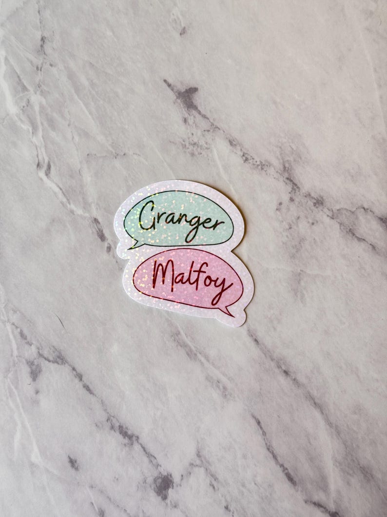 May include: Two speech bubble stickers with glitter. The top sticker is light blue with the word "Granger" in dark blue. The bottom sticker is pink with the word "Malfoy" in dark red.
